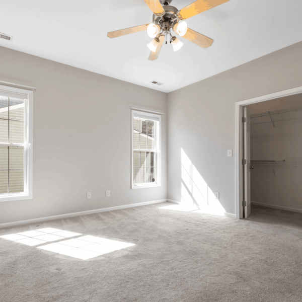 Empty bedroom featuring a ceiling fan and large windows with sunlight