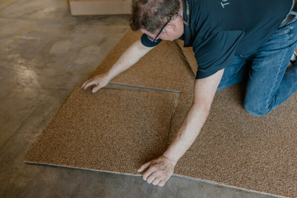 Person laying down carpet tiles on a concrete floor
