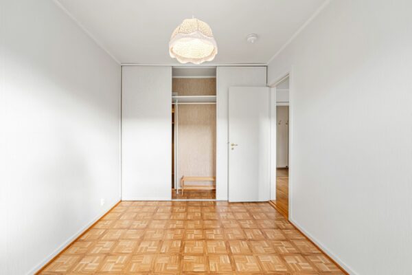 A spacious, empty room featuring a wooden floor and a modern pendant light.