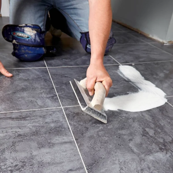 Close-up of a man's hand applying grout to floor tiles with a trowel
